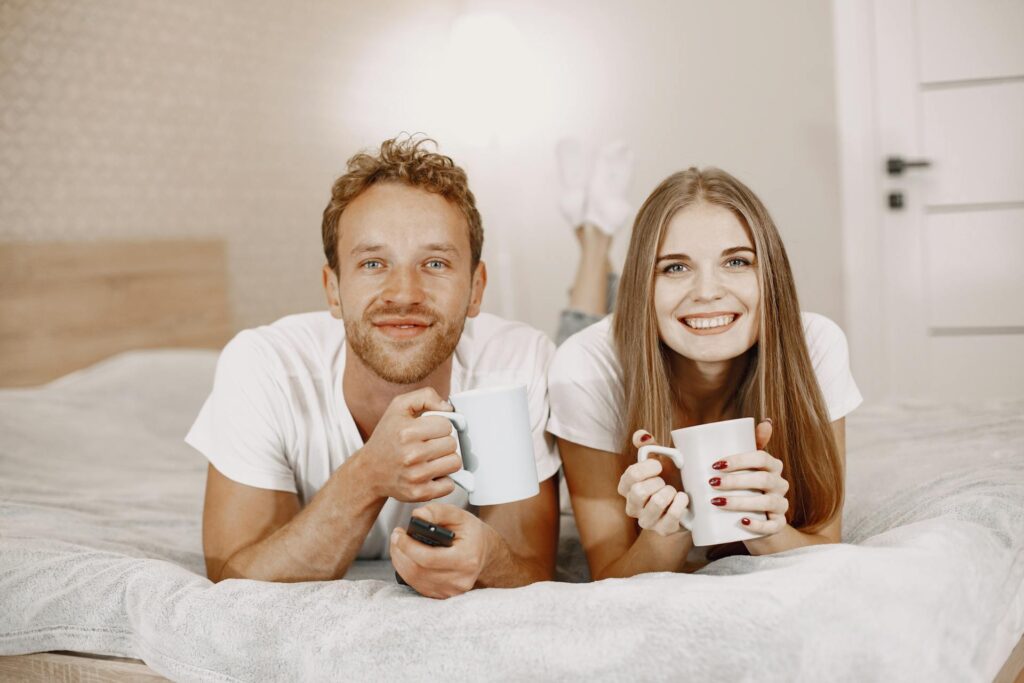 Couple lying on bed holding coffee mugs